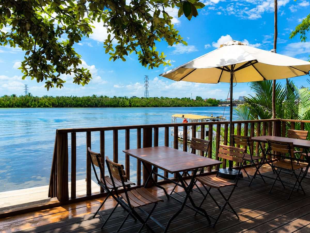 A table set on the riverside deck beneath a white parasol, looking out over the water